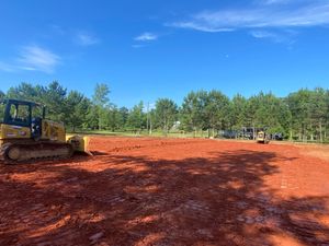 A bulldozer is moving dirt in a field with trees in the background.