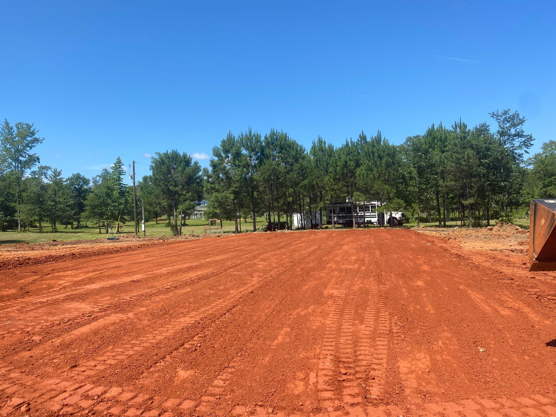 A large dirt field with trees in the background and a bulldozer in the foreground.