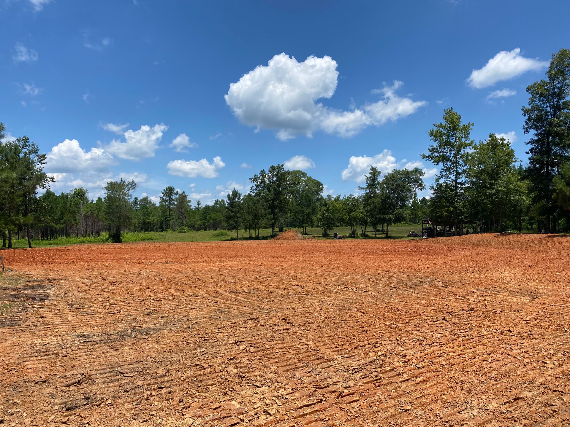 A large empty field with trees in the background and a blue sky with clouds.