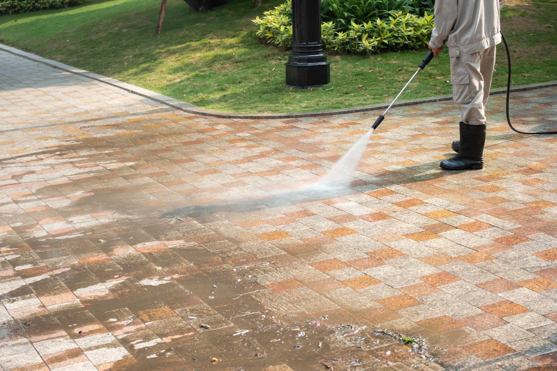 Person pressure-washing a brick walkway outdoors, with white spray cleaning the pavement