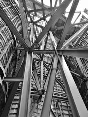 Black and white view looking up into a steel structure with intersecting beam
