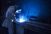 Welder in protective gear working with sparks and bright light in a dark workshop.