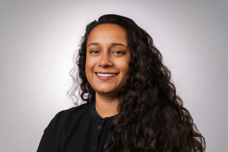 Woman with braided hair smiling, wearing a blue top, against a gray background.