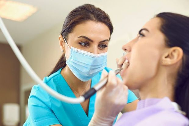 A woman is sitting in a dental chair with a dentist in the background.
