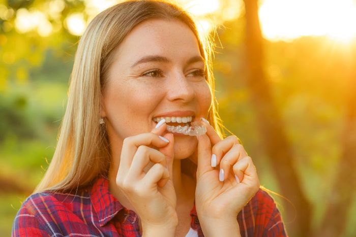A woman is holding a clear braces in her mouth.