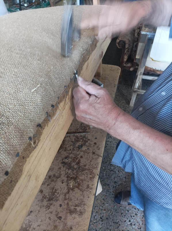 Persona che pianta chiodi in una cornice di legno ricoperta di tela di iuta. Lavora su un banco da lavoro.