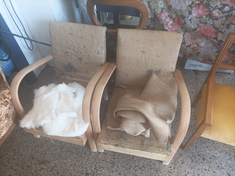 Due poltrone in legno in cattivo stato, con imbottitura e tessuto a vista, in un ambiente interno.
