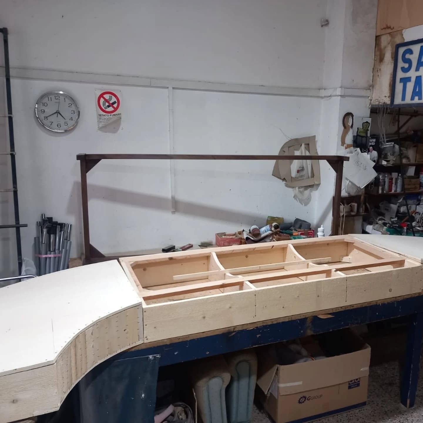 Un banco da lavoro per la lavorazione del legno con un pezzo di legno curvato parzialmente costruito, all'interno di un'officina.