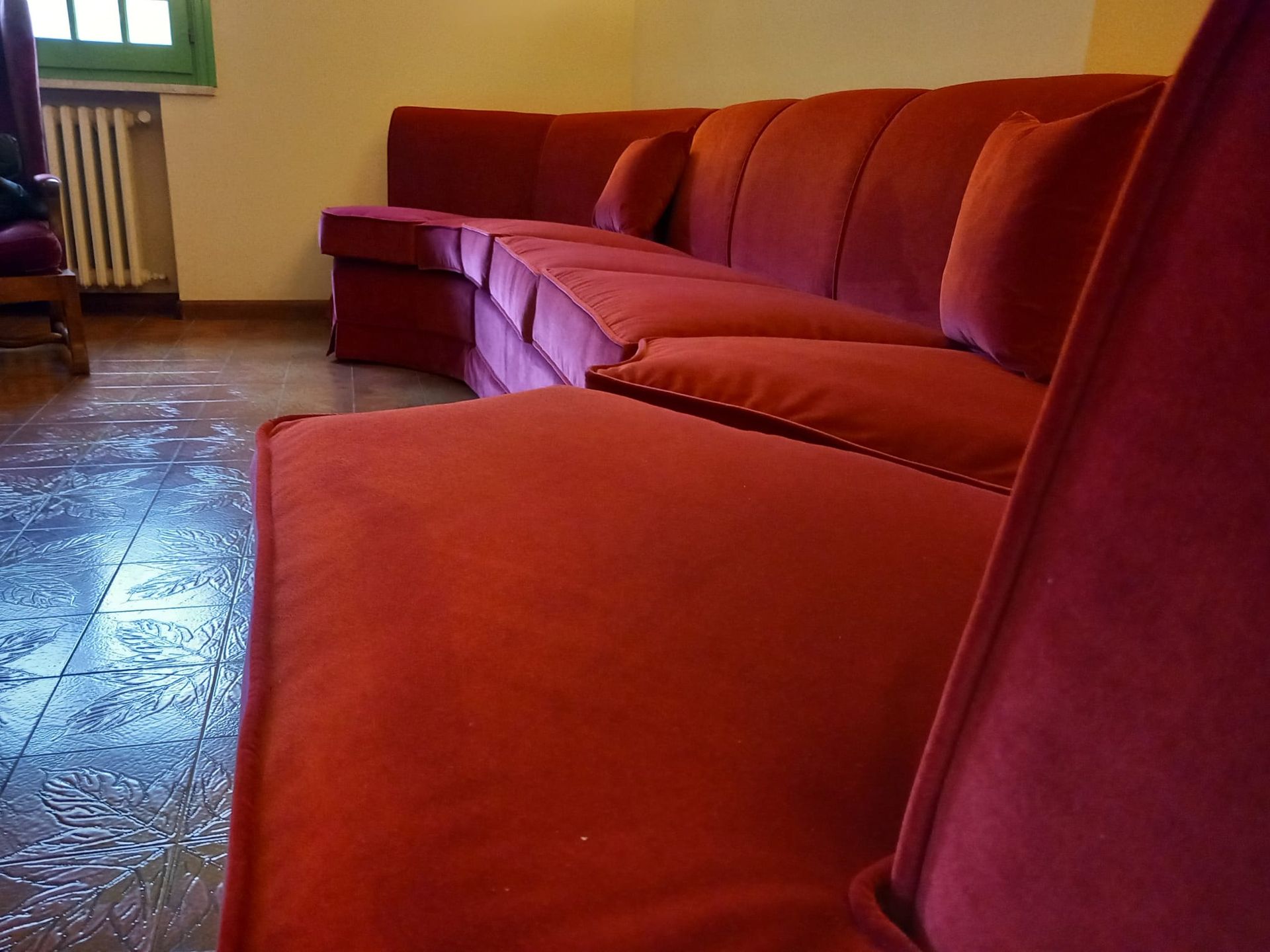 Divano componibile in velluto rosso in una stanza con pavimenti in legno e un termosifone.