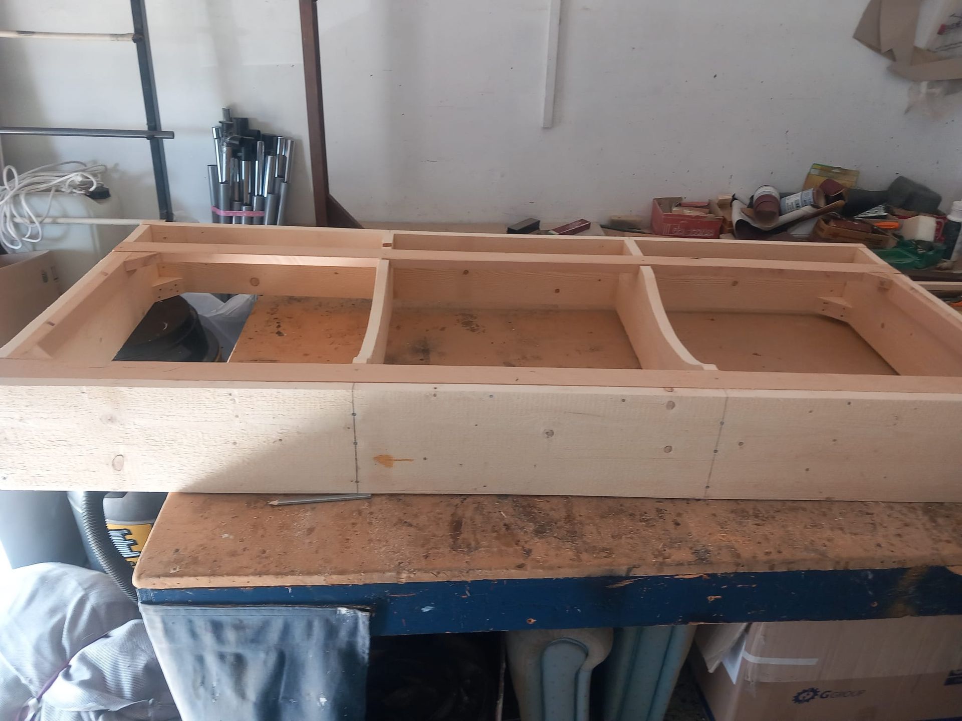 Telaio in legno con scomparti curvi, probabilmente utilizzato per costruire un modello o per riporre oggetti su un banco da lavoro.