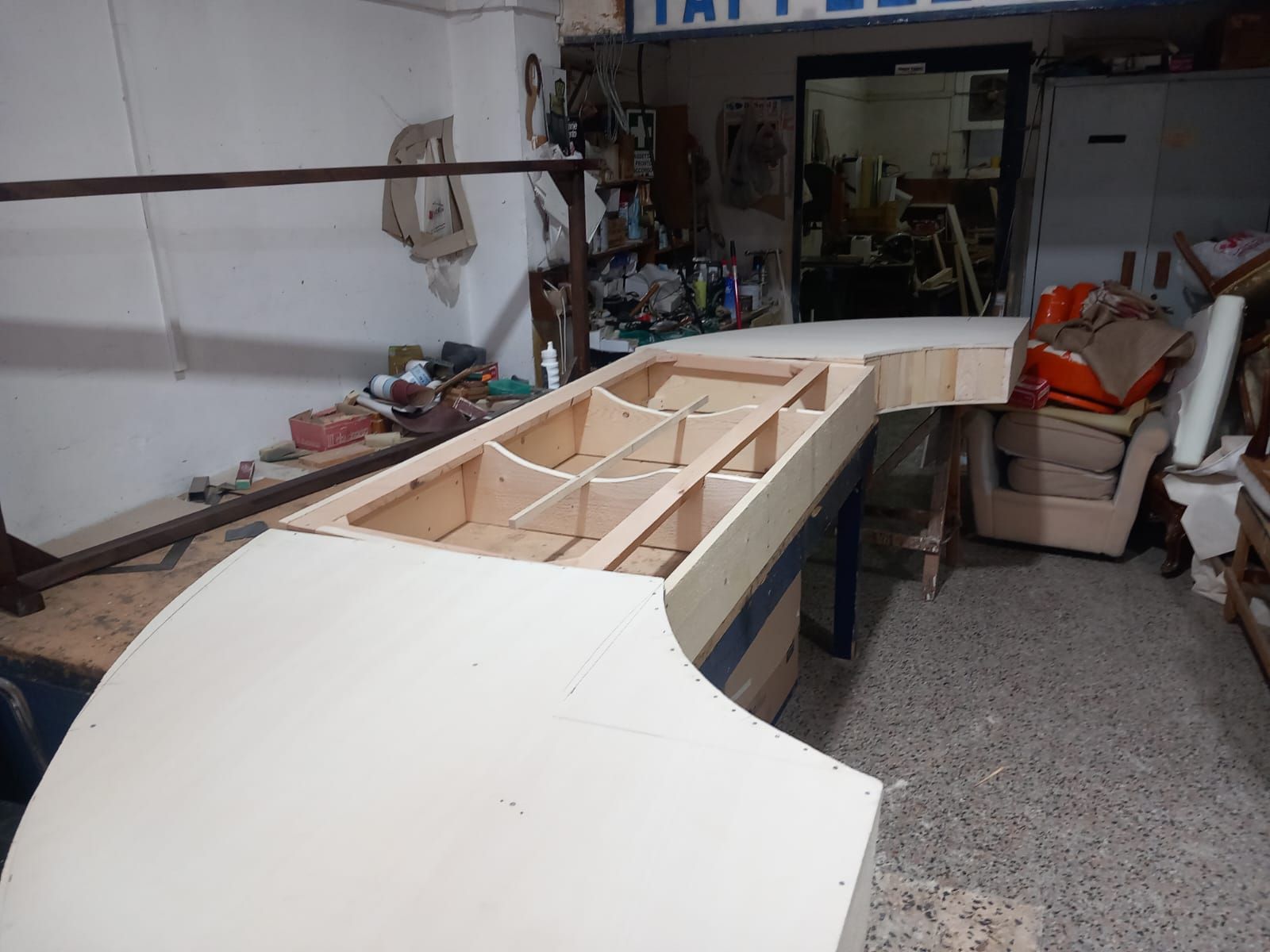 Piano di lavoro in legno in costruzione all'interno di un laboratorio, caratterizzato da una struttura a mobile aperto con più scomparti.