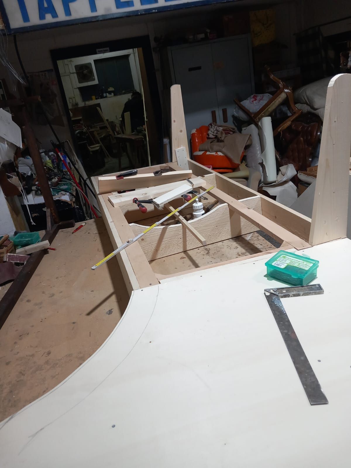 Un mobile in legno parzialmente costruito in un laboratorio, con attrezzi e materiali sparsi ovunque.