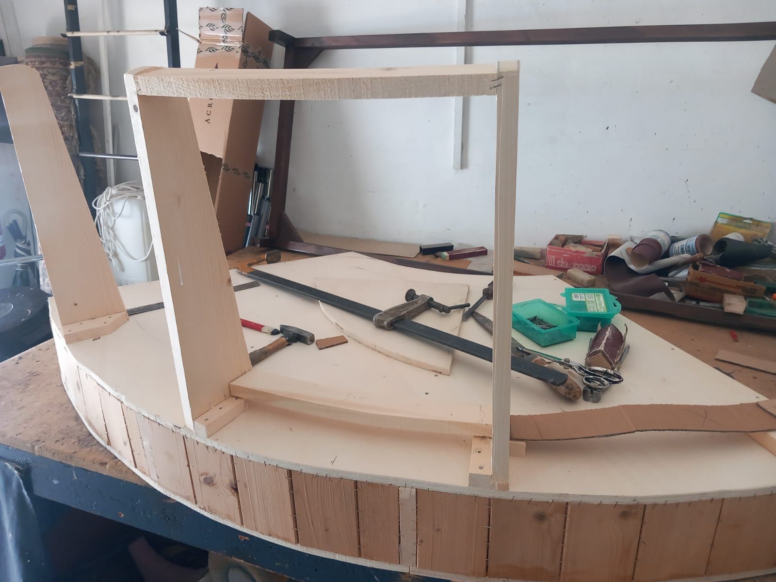 Telaio di una barca in legno in costruzione in un'officina, che mostra lo scafo, la struttura interna parziale e gli attrezzi.