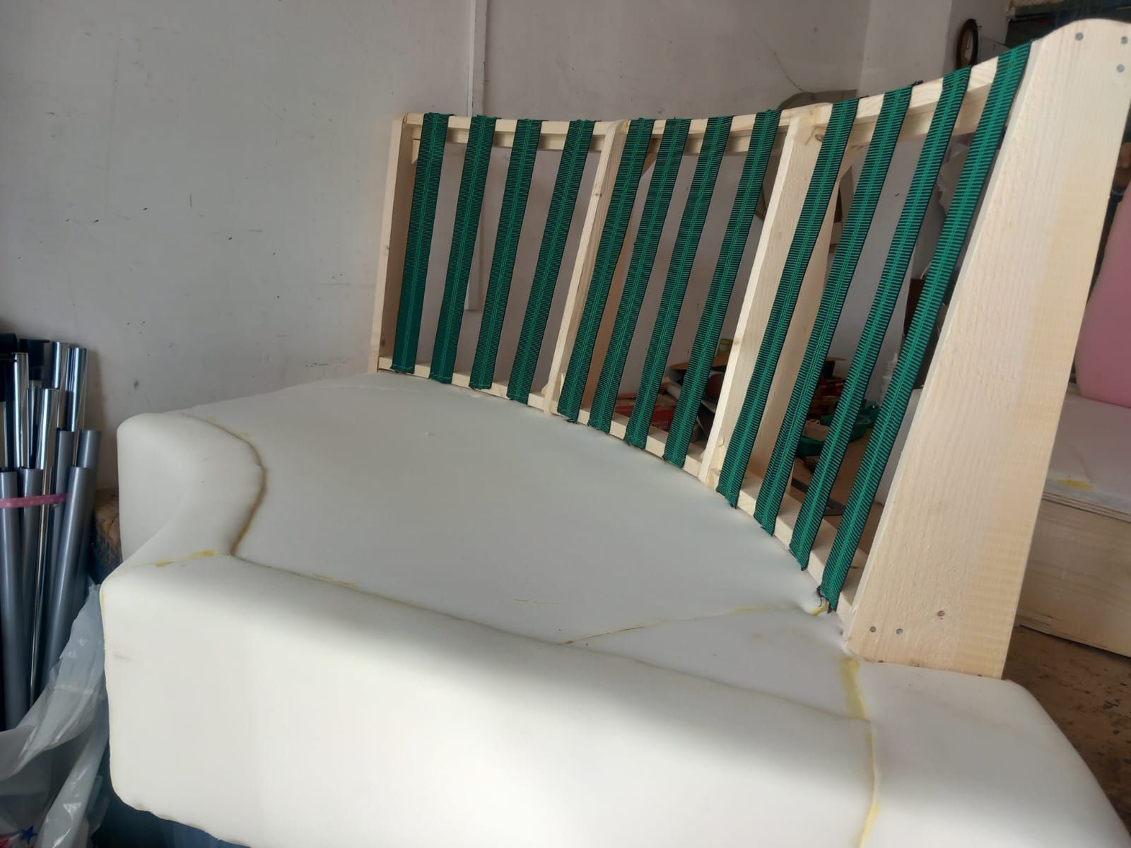 Divano grezzo con seduta curva in schiuma e schienale in legno con corda verde. L'ambiente sembra quello di un laboratorio.