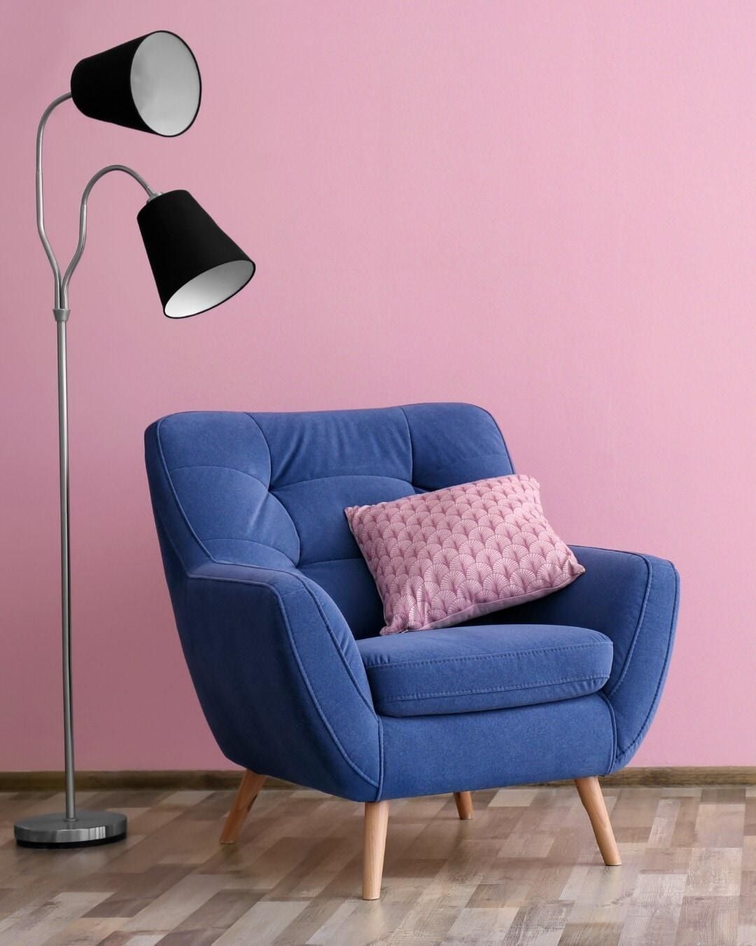 Poltrona blu con cuscino rosa accanto a una lampada da terra nera e argento contro una parete rosa.