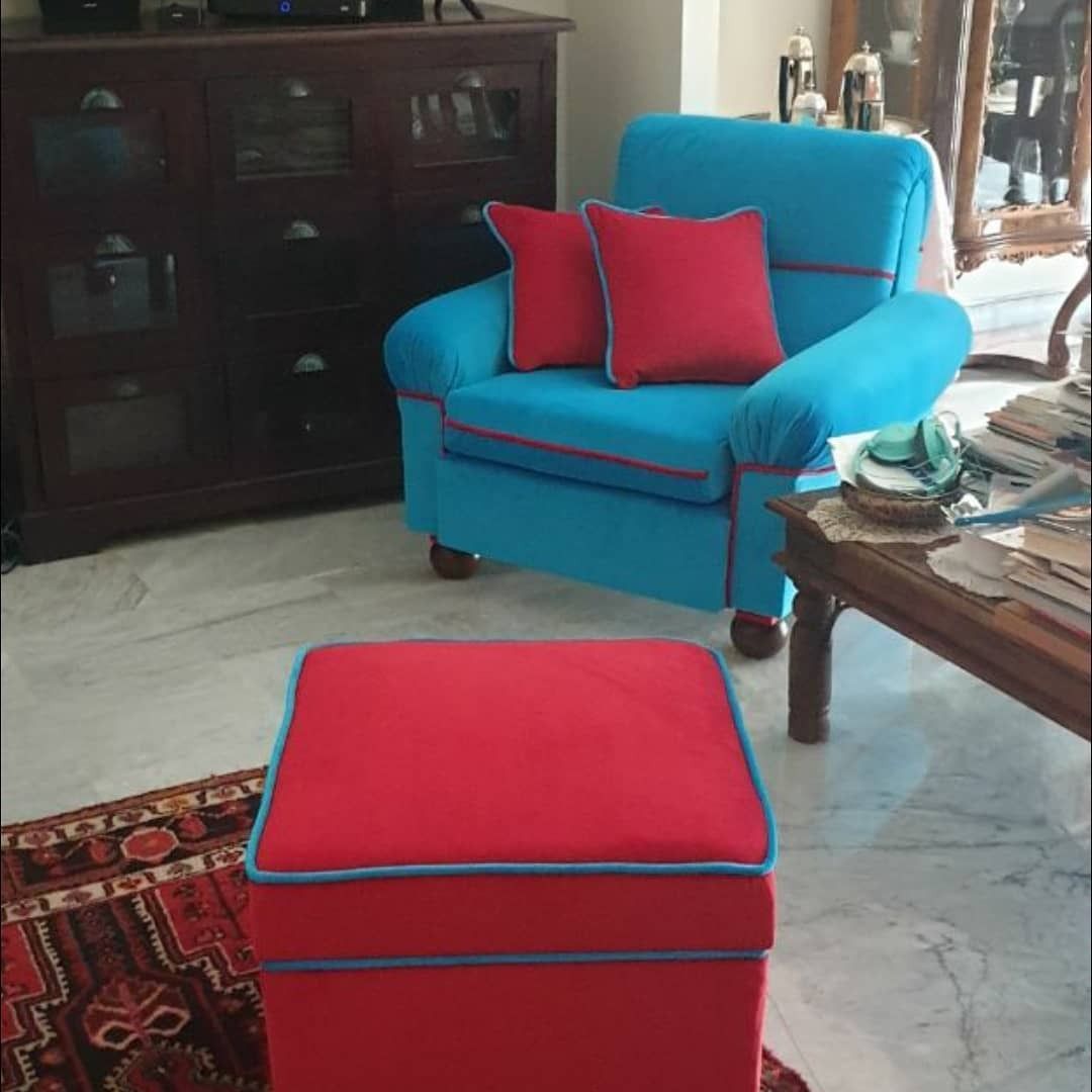 Poltrona blu brillante con cuscini rossi e pouf rosso coordinato in soggiorno. Sullo sfondo, un mobile in legno scuro.