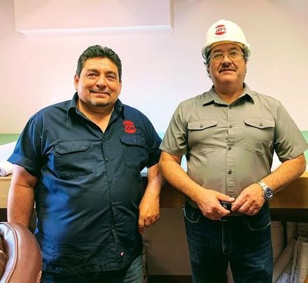 Two men wearing hard hats are posing for a picture