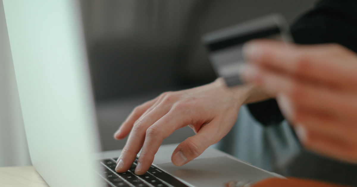 Person typing on laptop while holding a credit card, highlighting digital buying behavior and purchase intent.