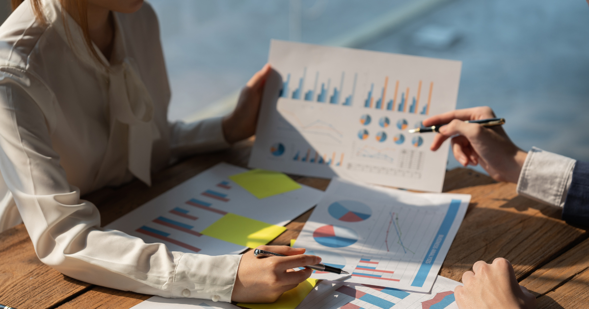 Two professionals analyzing colorful charts and graphs on paper during a data-driven business meeting.