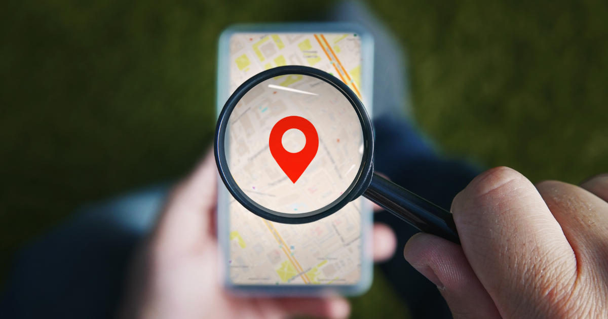 Hand holding a magnifying glass over a phone map with a red location pin icon, symbolizing local search focus.