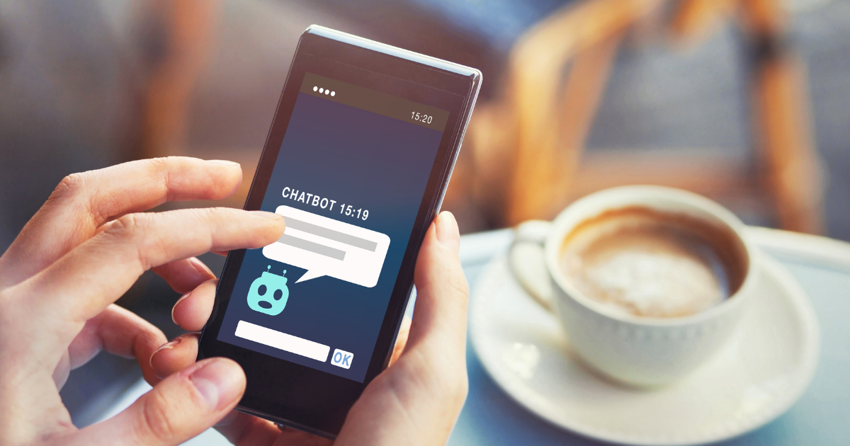A person interacts with a mobile app using chatbot solutions while enjoying coffee at a cozy café table.