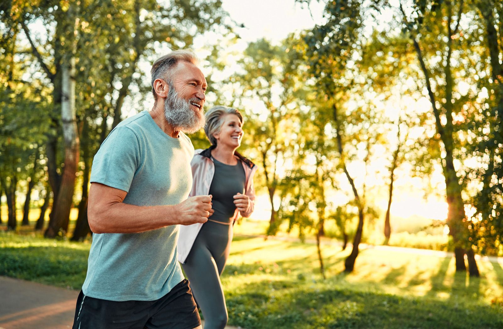 Zwei Personen joggen in einem sonnenbeschienenen Park zur goldenen Stunde.