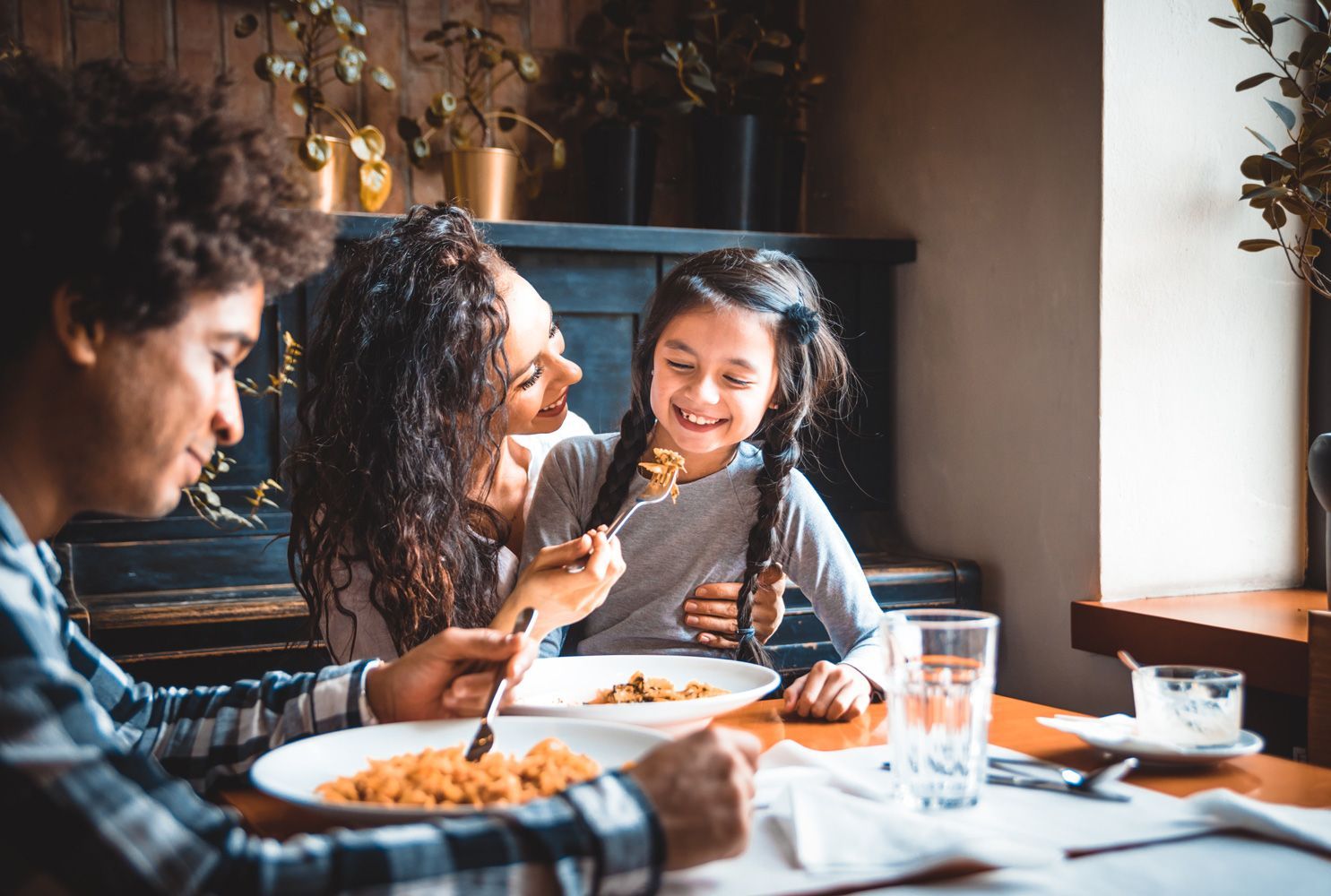 Family sharing a meal at a dining table, smiling and chatting in a warm, sunlit room.