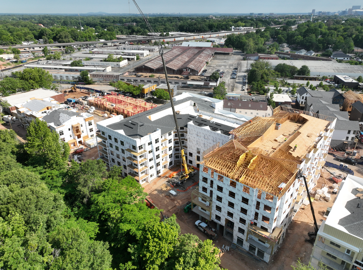 Aerial view of a construction site with white apartment buildings, cranes, and green trees nearby.
