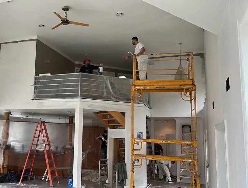 Painters working on interior walls, using scaffolding and ladders in a two-story space.