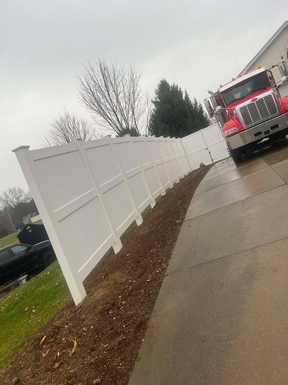 A red truck is parked next to a white fence.