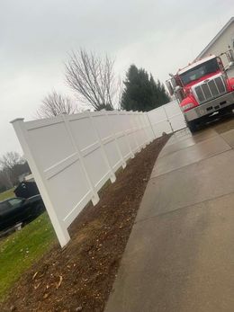 A red truck is parked next to a white fence.