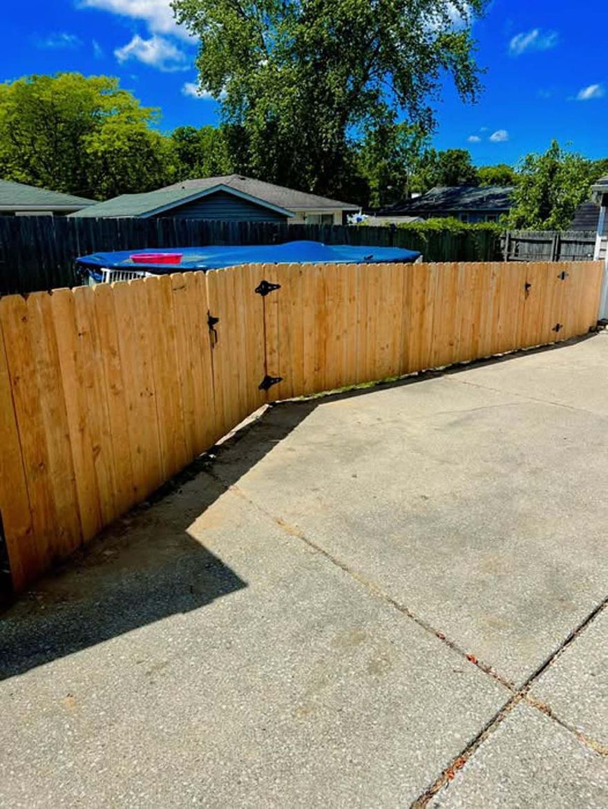 A wooden fence is sitting on top of a concrete driveway next to a house.