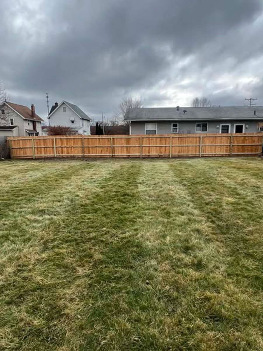 A backyard with a wooden fence and a lush green lawn.