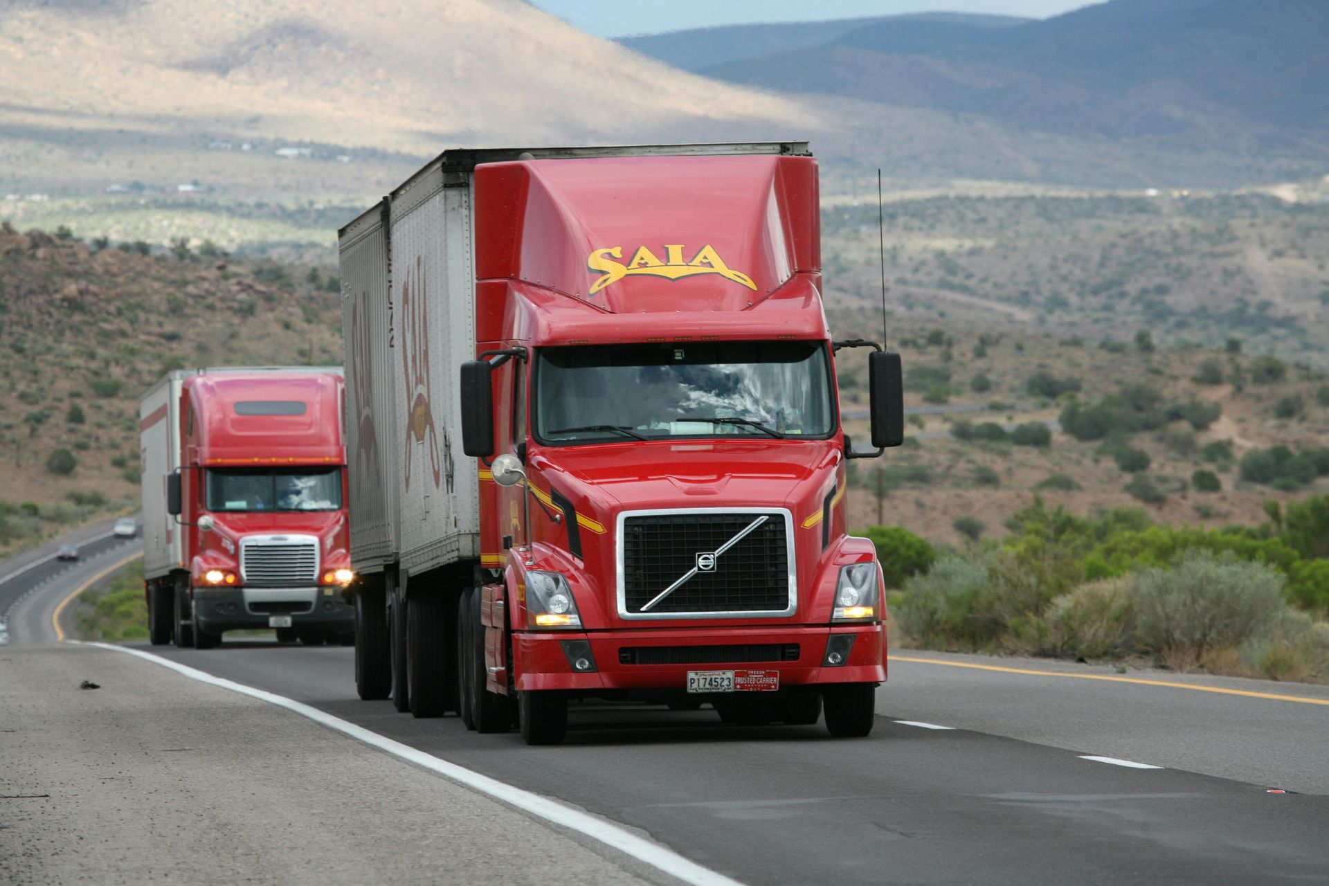 Two red volvo semi trucks are driving down a highway