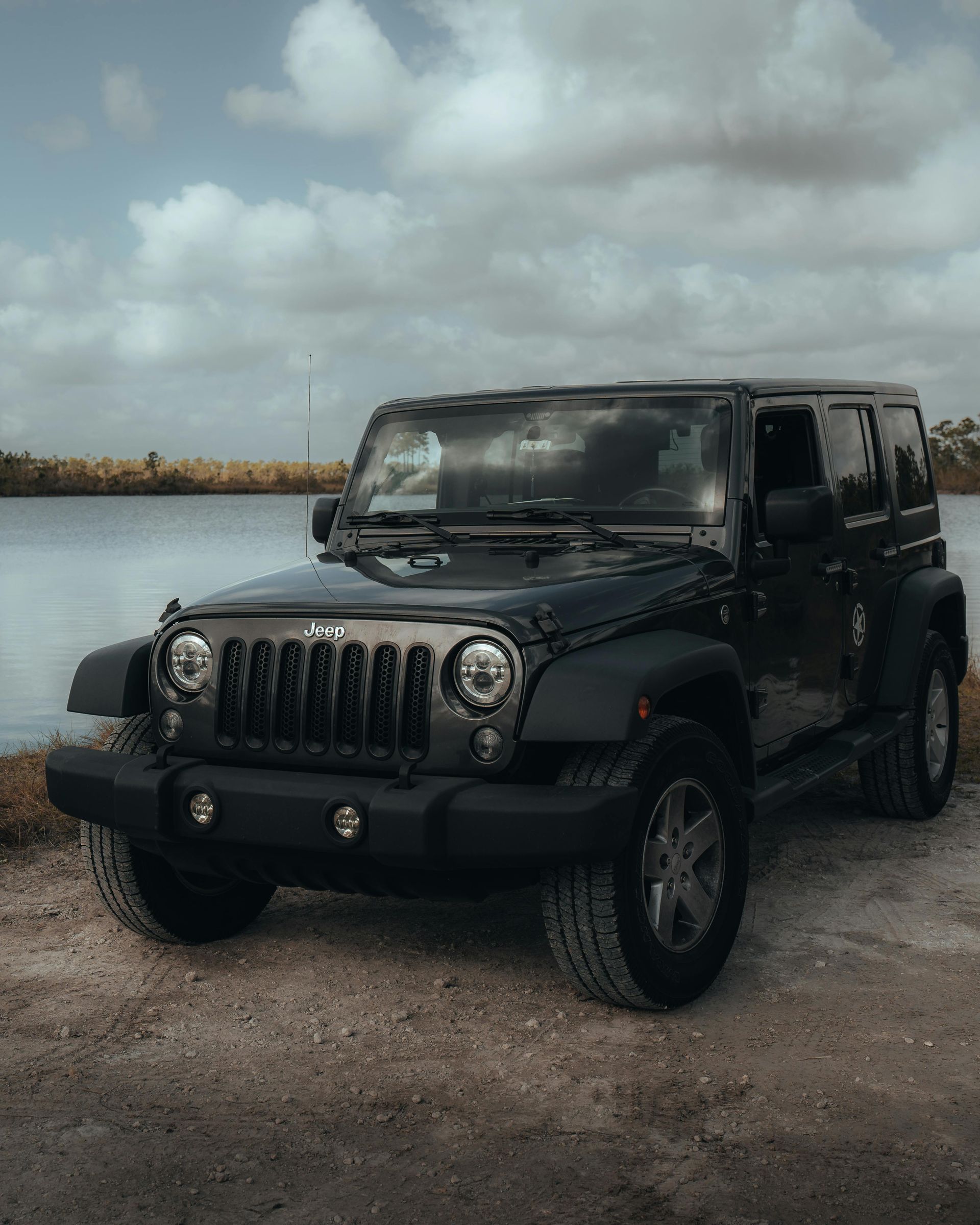 A black jeep is parked next to a body of water.