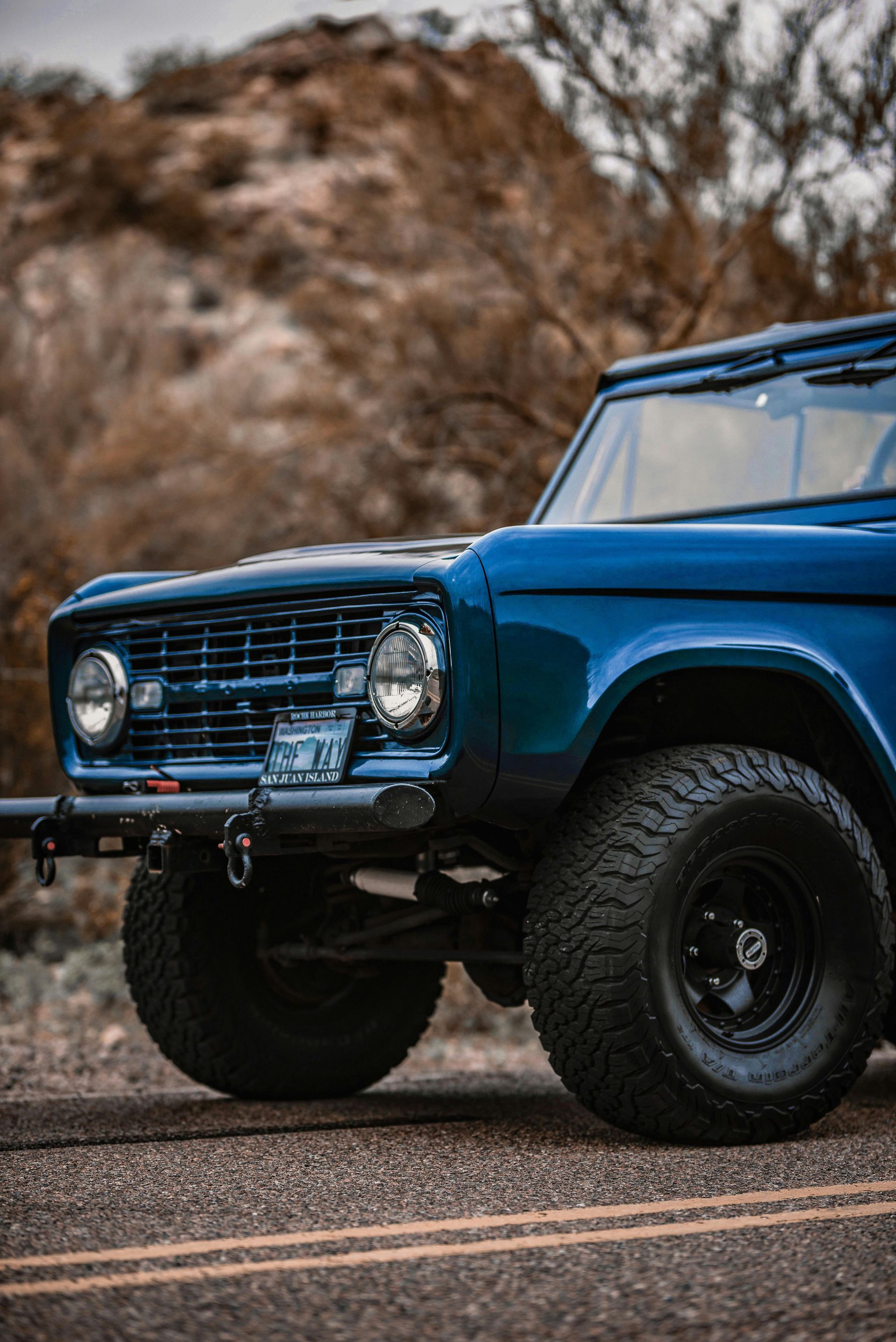 A blue ford bronco is parked on the side of the road.