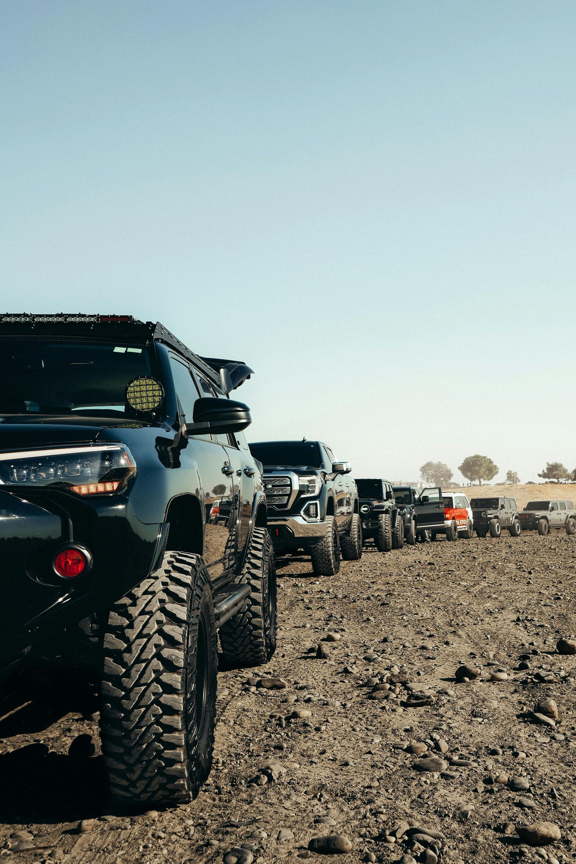A row of trucks are parked in a dirt field.
