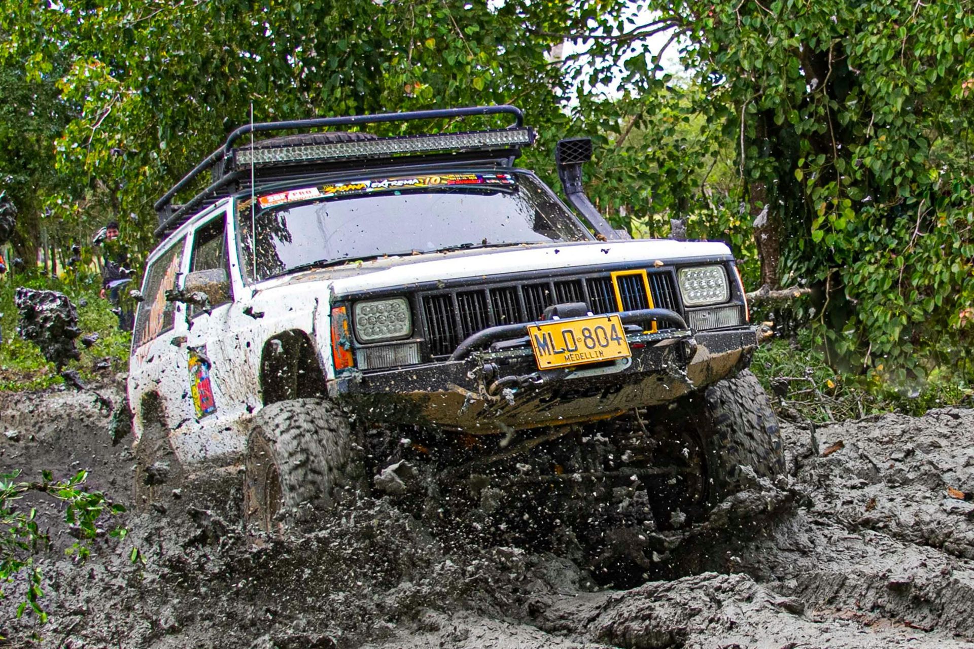 A white jeep is driving through a muddy area.