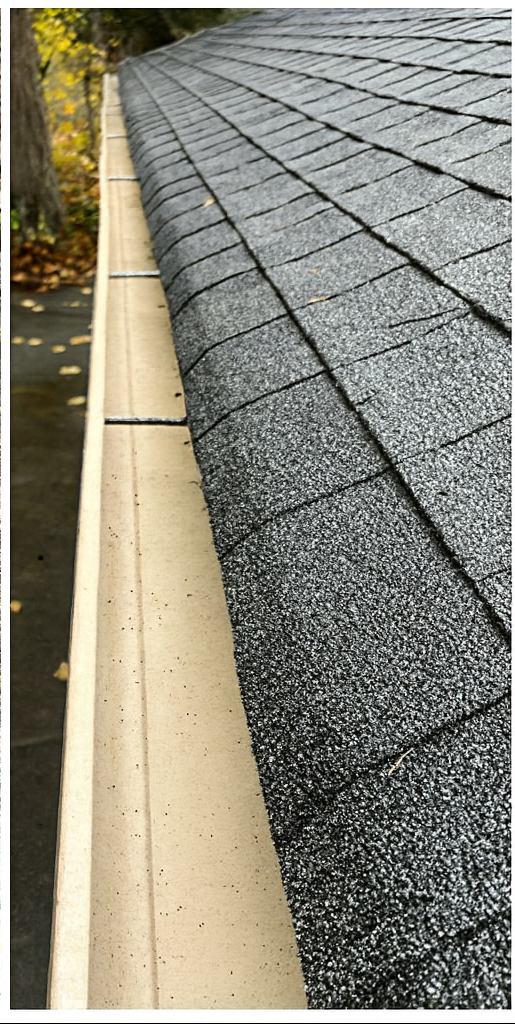 A roof with dark gray shingles and a beige gutter along the side.