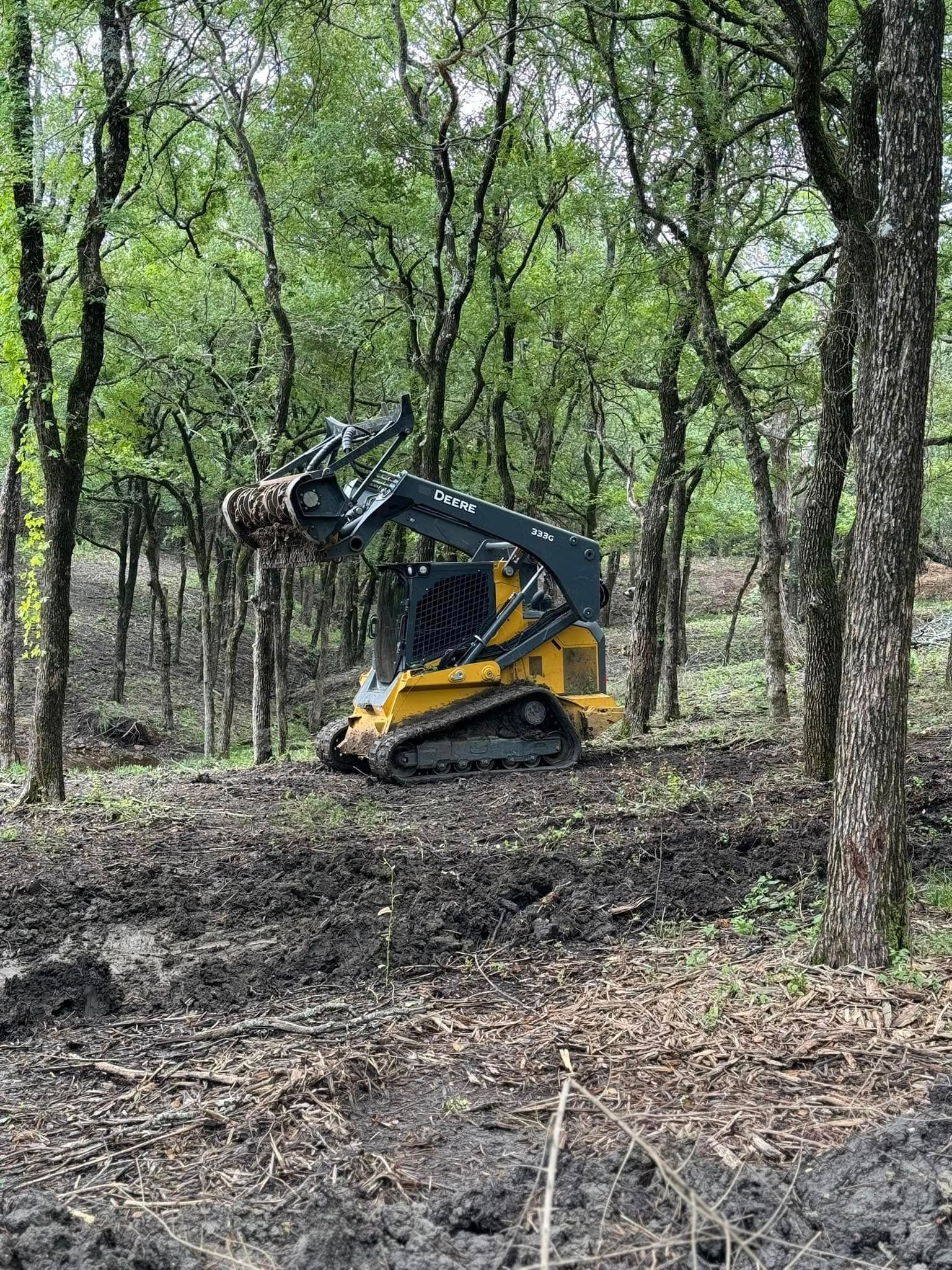 Yellow tracked skid steer in a muddy forest clearing.