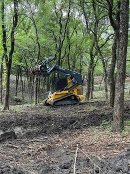 Yellow tracked skid steer in a muddy forest clearing.