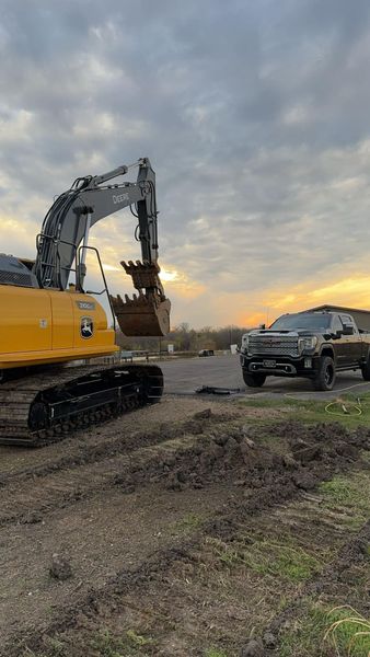 A yellow excavator and black pickup truck on a construction site under a cloudy sky.