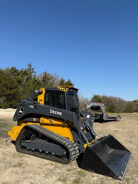 Yellow and black skid steer loader on a grassy field under a blue sky.