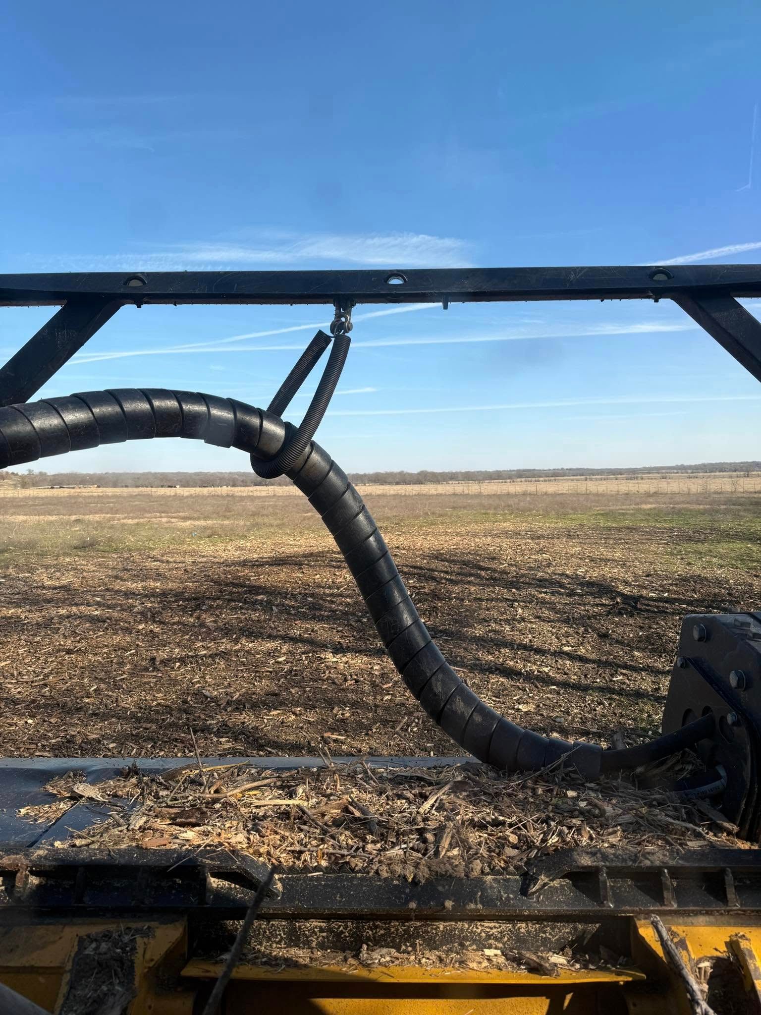 Black flexible hose and metal frame against a field and blue sky.
