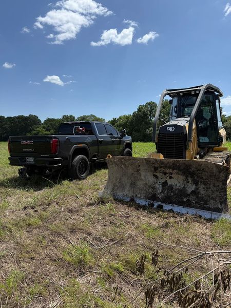 Black GMC truck and yellow bulldozer in a grassy field on a sunny day.