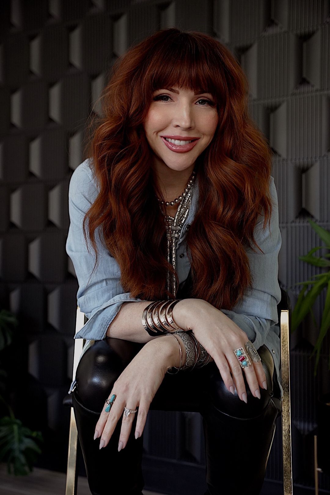 A woman with red hair is sitting in a chair with her hands on her knees.