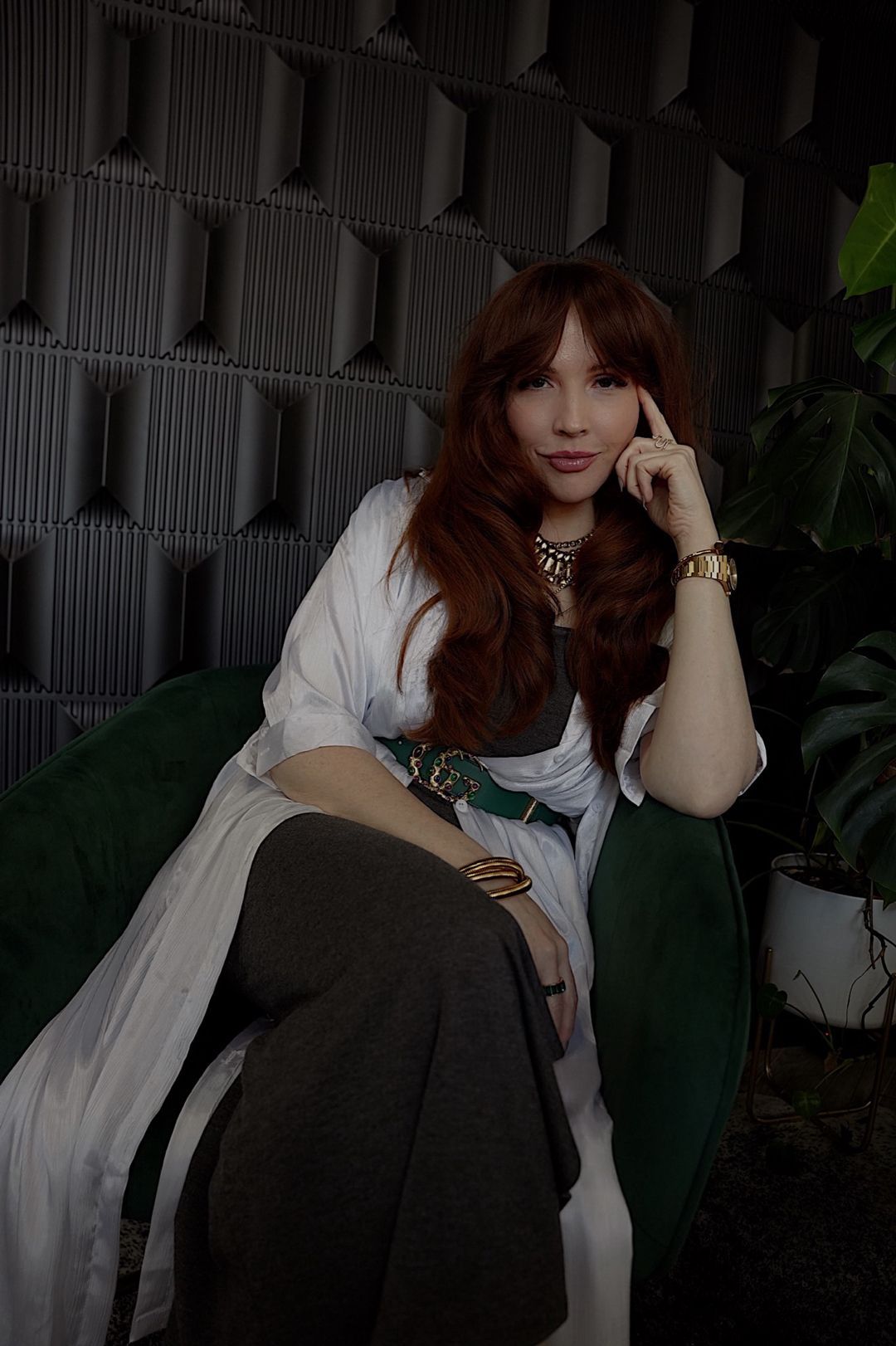 A woman is sitting in a green chair with her hand on her chin.