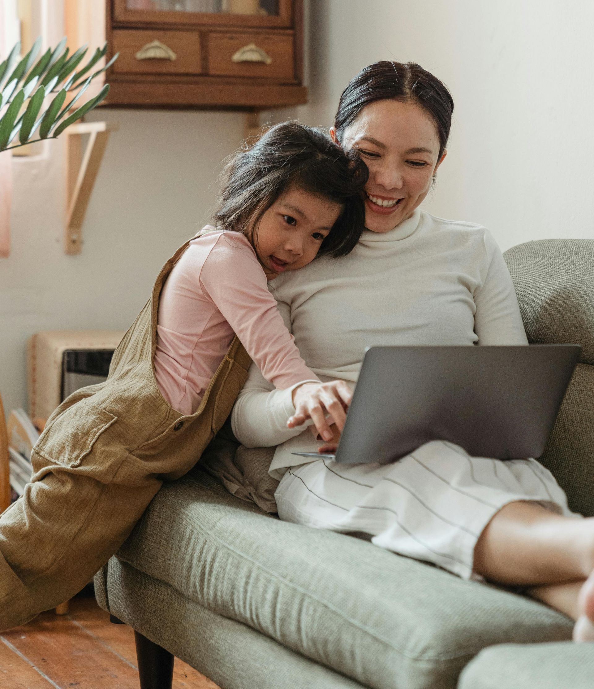 A woman and a little girl are sitting on a couch looking at a laptop.