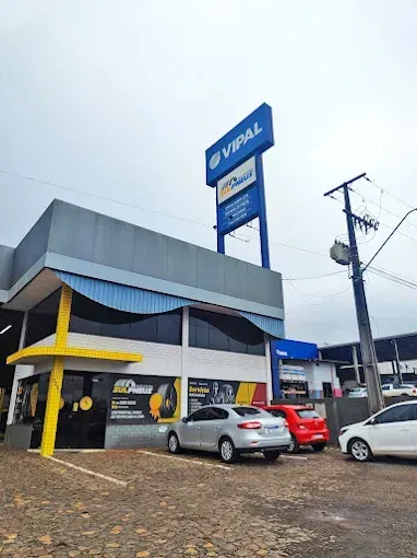 Um homem de macacão amarelo segura um pneu na frente de um carro.