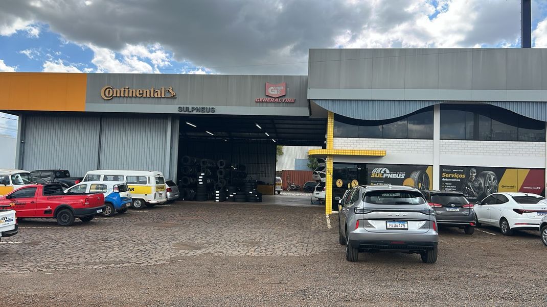 Um homem de macacão amarelo segura um pneu na frente de um carro.